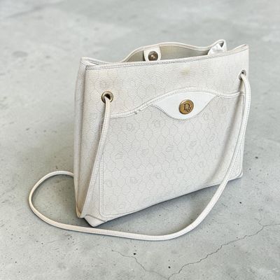 sac à main beige et blanc posé sur un sol en béton, muni d'une poignée et d'une bandoulière