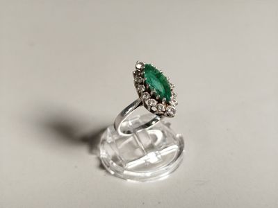 une image représentant une bague ornée d'une pierre verte posée sur un socle transparent