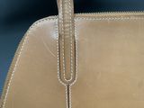 the handle of a tan purse with white stitching on it