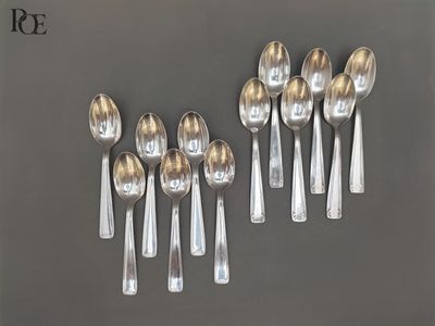 six cuillères en argent sont disposées en rang sur une surface grise