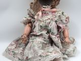 an old fashioned doll sitting on a white surface wearing a dress and hat