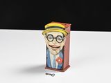 figurine de bande dessinée représentant un homme à lunettes et coiffé d'un chapeau, dans une boîte