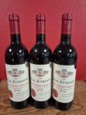 Trois bouteilles de vin sont posées sur une table en bois devant un mur rouge.