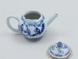 a blue and white teapot with a lid next to a cookie