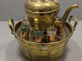 une théière en laiton avec des tasses à thé posées sur un plateau, le tout sur une table