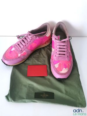 des baskets roses et vertes posées sur un sac vert, lui-même posé sur une surface blanche