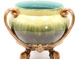 a green and gold vase on a stand on a white background