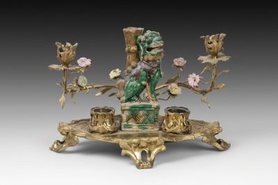 une image représentant une figurine dorée et verte ornée de fleurs, posée sur un socle