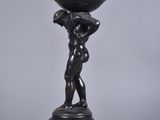 an antique bronze statue of a boy holding a globe on his shoulders