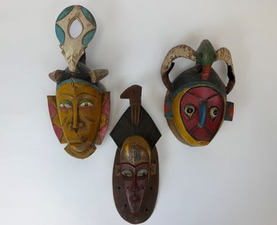 trois masques en bois accrochés au mur d'une pièce blanche