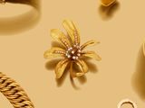 des bijoux en or sur fond beige, avec une broche en forme de fleur en or et une chaîne en or
