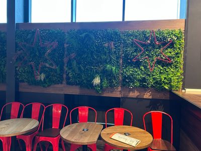 tables and chairs in a restaurant with a wall of plants behind them
