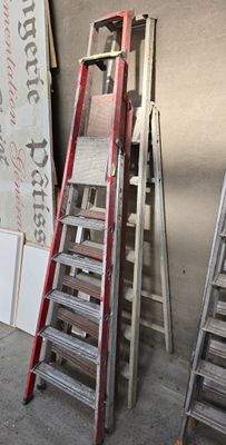 Plusieurs échelles sont alignées contre un mur dans un garage.