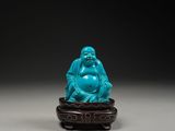 une figurine en jade bleu représentant un Bouddha rieur, posée sur un socle