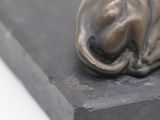 a bronze statue of a cat laying on a black block