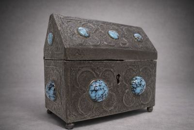 une boîte en argent contenant des pierres bleues, posée sur une surface grise