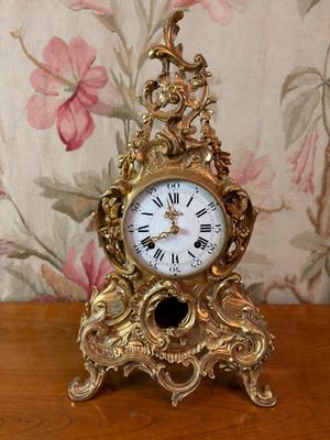 une horloge en or posée sur une table en bois, avec un papier peint à motifs floraux en arrière-plan