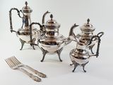 a silver tea set on a table with a fork and knife