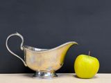a silver gravy with an apple next to it