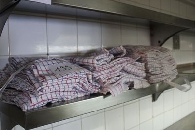 Des serviettes sont empilées sur une étagère métallique dans une cuisine, à côté d'un évier.