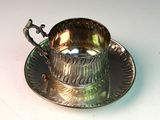 a silver cup and saucer sitting on a plate