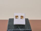 a pair of gold stud earrings sitting on top of a marble block