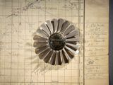une fleur en métal posée sur un morceau de papier, lui-même posé sur un autre morceau de papier