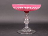 un saladier en verre rose posé sur un socle en verre, lui-même posé sur une surface noire