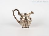 an old silver pitcher with a handle on a white surface