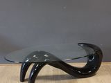 a black glass coffee table with curved legs and a curved glass top