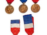 Plusieurs médailles sont exposées sur un fond blanc, accompagnées de rubans rouges, blancs et bleus