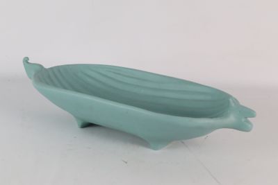 un petit bol vert muni d'une longue anse, posé sur une surface blanche