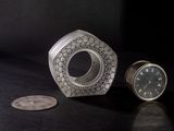 a silver clock sitting next to a coin on a table