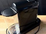a black coffee maker on a wooden table with a black background