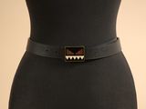 une femme vêtue d'une robe noire et d'une ceinture noire ornée d'un motif géométrique