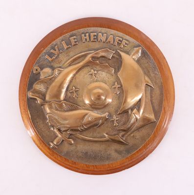 une médaille de bronze posée sur une plaque en bois, elle-même posée sur un fond blanc