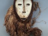 un masque marron et blanc accroché à un mur gris