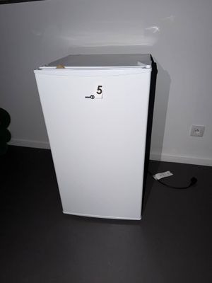 un petit réfrigérateur blanc dans le coin d'une pièce