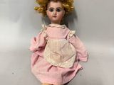une vieille poupée aux cheveux blonds et vêtue d'une robe rose, assise sur une surface blanche