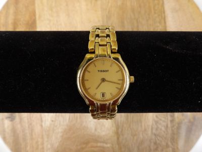 une montre en or posée sur un anneau noir, sur une table en bois