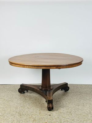 une table ronde en bois munie de roulettes, posée sur un sol recouvert de moquette