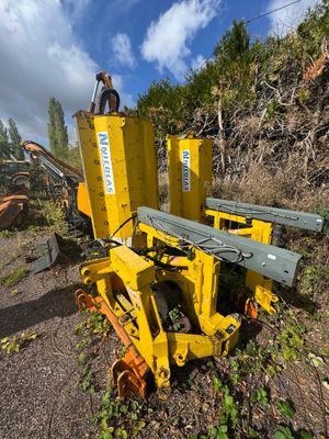un homme debout sur une machine jaune, à côté d'un tas d'arbres
