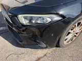 the front end of a black car with a dent in it ' s bumper