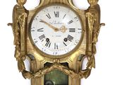 a gold clock on the wall with roman numerals on it