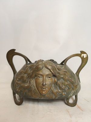 sculpture en bronze représentant le visage d'une femme, sur une plaque en laiton