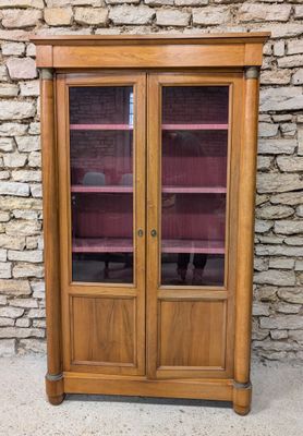 a wooden cabinet with glass doors and shelves in front of a stone wall