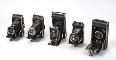 cinq vieux appareils photo sont alignés sur une surface blanche