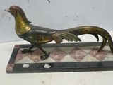 statue d'un coq doré posée sur un socle en marbre, elle-même posée sur une table blanche