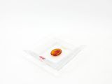 une pierre orange dans un bol en verre transparent posé sur une surface blanche