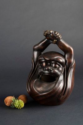 une statue en bronze représentant un homme souriant tenant une pomme de pin